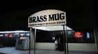 Entrada nocturna del The Brass Mug con letrero iluminado