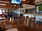 Interior del pub con barra, mesas, sillas y televisión colgada