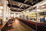 Interior del bar con mostrador largo, taburetes rojos y estanterías de bebidas