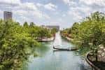 Canal rodeado de árboles verdes con puentes pequeños y vista hacia el centro de la ciudad