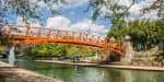 Puente naranja sobre el canal con vegetación densa y cielo parcialmente nublado