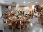 Interior del salón de eventos con mesas dispuestas para banquete, sillas doradas y decoración floral central