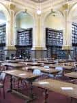 Interior histórico de la sala de lectura con estanterías altas, arcos decorativos y mesas de estudio