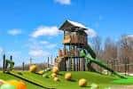 Área de juegos infantiles con torre de madera y tobogán verde en un día soleado