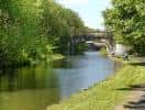 Puente de piedra sobre el canal rodeado de vegetación densa y sendero peatonal