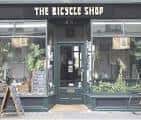 Fachada exterior de The Bicycle Shop con letrero y plantas decorativas