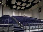 Interior del auditorio con asientos azules y sistema de iluminación en el techo