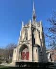 Fachada principal de la capilla con puerta roja y aguja gótica bajo cielo azul