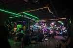 Ambiente nocturno con luces de neón y público sentado en el área de entretenimiento del lugar