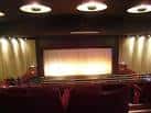 Sala principal del cine con butacas rojas, cortinas doradas y escenario con telón cerrado