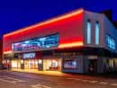 Exterior nocturno del Savoy Cinema con iluminación roja neón y letrero luminoso visible