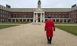 Patio interior del Royal Hospital Chelsea con un guardián en uniforme rojo caminando hacia el monumento central