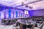 Interior del salón de eventos con mesas redondas, sillas y escenario iluminado con luces púrpuras