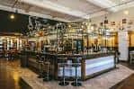 Interior del bar con mostrador largo, estanterías de botellas y taburetes altos