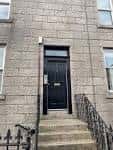 Fachada exterior del edificio con puerta principal negra y escalera de acceso