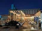 Vista nocturna del patio exterior de Broken Clock Brewing con mesas y luces decorativas