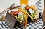 Plato de tacos servidos en bandeja metálica sobre mesa a cuadros