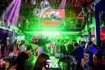 Vista interior del local con luces verdes, discoteca y gente bailando