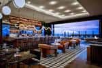Interior del bar con barra de madera y vistas panorámicas al atardecer