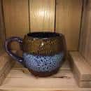 Taza de cerámica artesanal con esmalte azul y marrón sobre estantería de madera