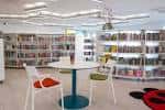 Interior luminoso de la biblioteca con estanterías curvas, mesas redondas y sillas coloridas