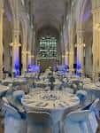 Sala principal preparada para una recepción con mesas redondas cubiertas de blanco y sillas decoradas
