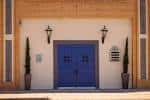 Detalle de la puerta principal azul con faroles laterales y plantas decorativas