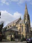Fachada exterior de la iglesia con su característica aguja y mampostería de piedra
