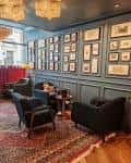 Sala de estar interior con paredes azules, cuadros enmarcados y sillones oscuros