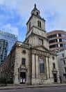 Fachada lateral de la iglesia en un día soleado con edificios modernos al fondo