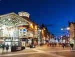 Plaza de Briggate al atardecer con edificio moderno iluminado y ambiente urbano