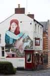 Fachada lateral del establecimiento con mural artístico de una figura femenina
