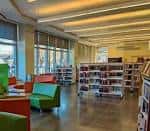Interior luminoso de la biblioteca con estanterías organizadas, mobiliario colorido y espacios abiertos para lectura