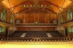 Interior del auditorio principal con asientos en gradas y techo de madera curvado