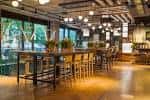 Interior del bar con barra alta, iluminación cálida y grandes ventanales