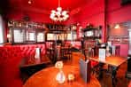 Interior del pub con decoración roja, mesas redondas, sillas tapizadas y lámparas colgantes