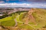 Vista panorámica de Holyrood Park con senderos y colinas verdes bajo cielo azul