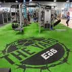 Interior del gimnasio The Yard Gym con suelo verde y logotipo visible