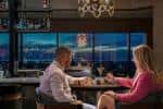 Pareja sentada en la barra con vista a la ciudad desde grandes ventanales