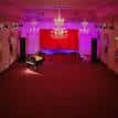 Escenario vacío de Bush Hall con cortina roja central y arañas de cristal bajo luz tenue
