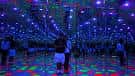 Sala de espejos e iluminación multicolor con público interactuando