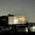 Vista nocturna de la pantalla del South Drive-In Theatre con coches aparcados frente a ella