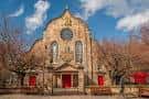 Vista exterior de la fachada principal de Canongate Kirk con su reloj circular y puertas rojas