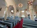 Interior de la iglesia mostrando el pasillo central con alfombra roja y bancos blancos bajo arcos