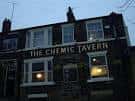 Fachada nocturna del The Chemic Tavern con letrero iluminado