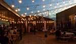 Vista del patio exterior de la cervecería con luces colgantes y mesas al atardecer