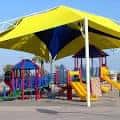 Área de juegos infantiles con estructuras coloridas y sombra amarilla
