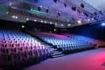 Interior del auditorio con butacas en gradas y escenario iluminado