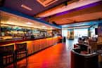 Interior del bar del hotel con barra larga, iluminación cálida y zona de asientos