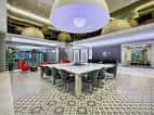 Sala de reuniones con mesa larga y sillas grises bajo lámparas circulares